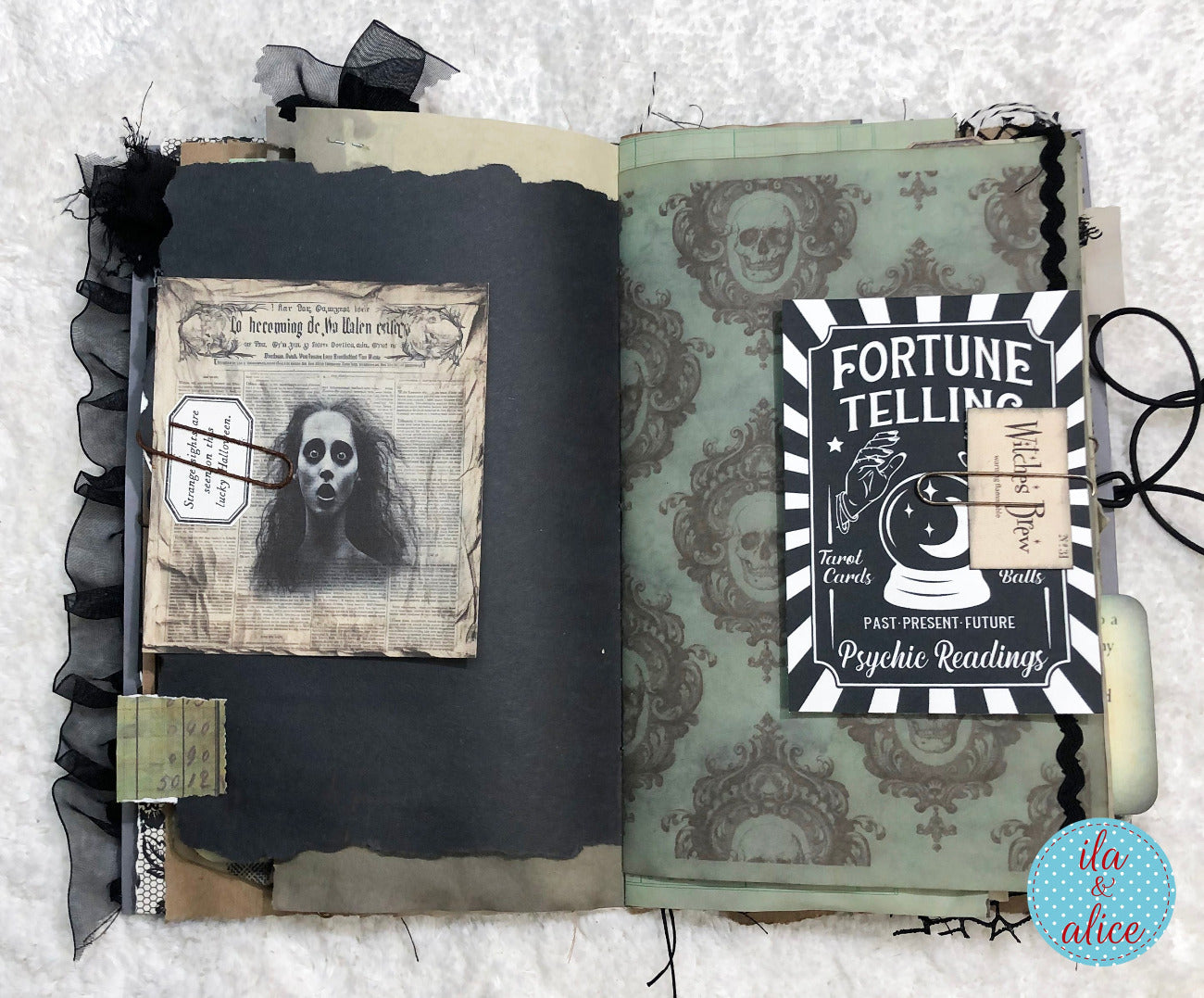 An open gothic-themed handmade journal or scrapbook album on a white textured fabric background. The left page is dark charcoal with black ruffled trim and a vintage-style skull card.