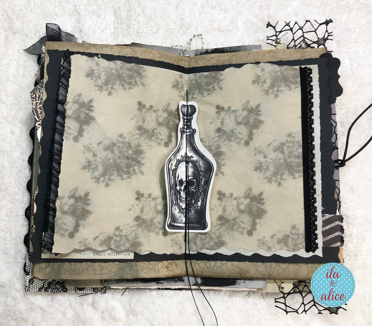 A handmade gothic scrapbook journal page featuring a vintage patterned background, black lace trim, and a central die-cut sticker of a skull inside a glass bottle. A blue circular 'it's alice' logo is visible in the bottom right corner.