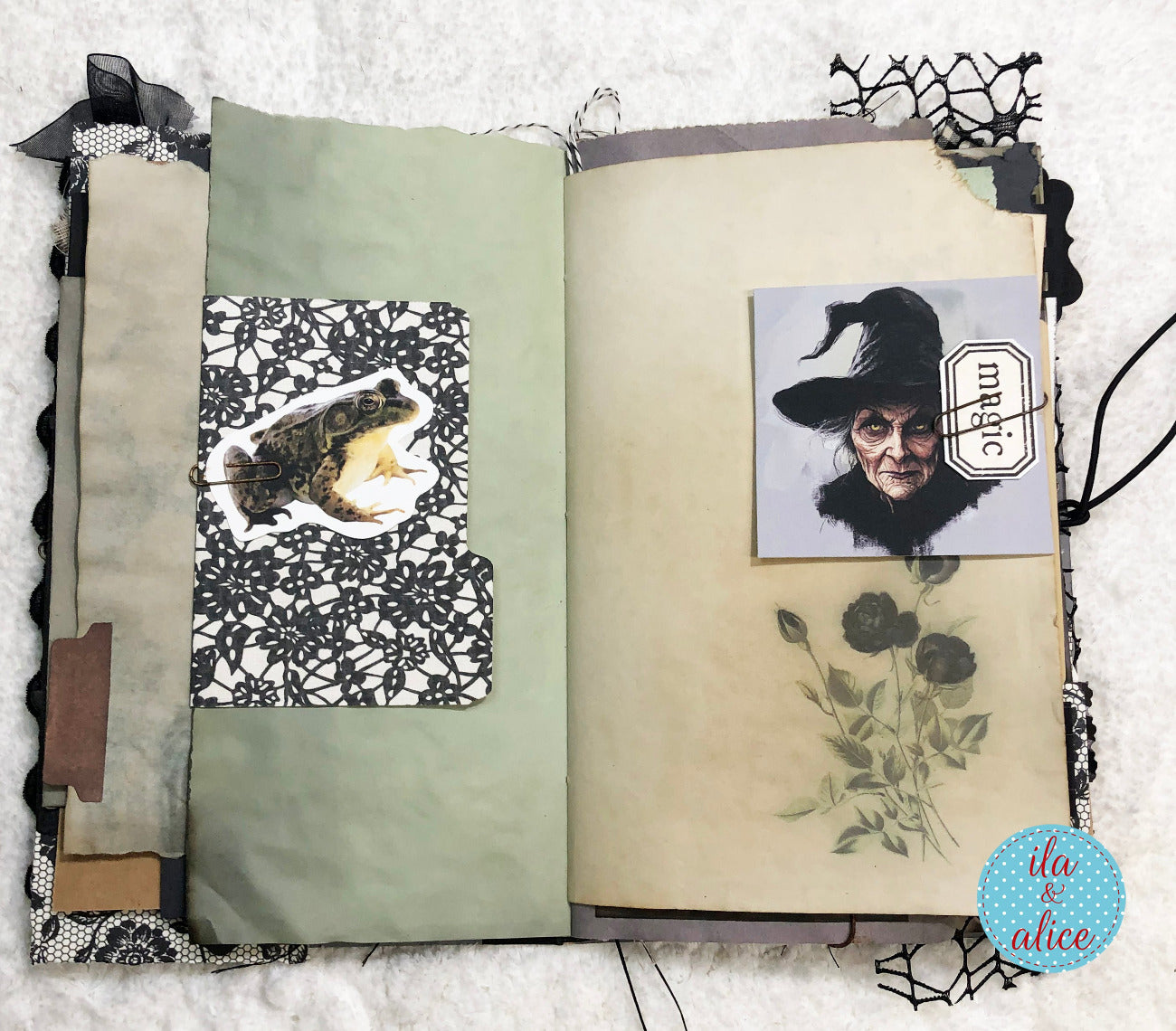 An open handmade scrapbook journal with layered pages, featuring a green card pocket with a toad illustration, a vintage-style portrait of a witch with a 'magic' label, and a floral print on the right page, set against a white textured background.