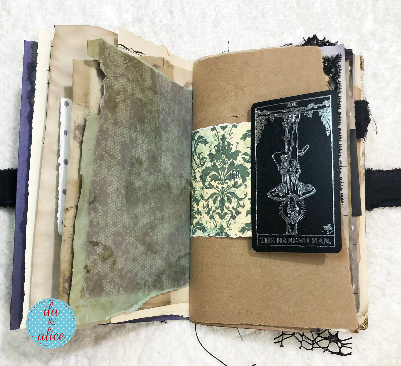 Handmade Eerie Halloween Gothic junk journal  with textured pages and a tarot card titled 'The Hanged Man' on a textured white background.