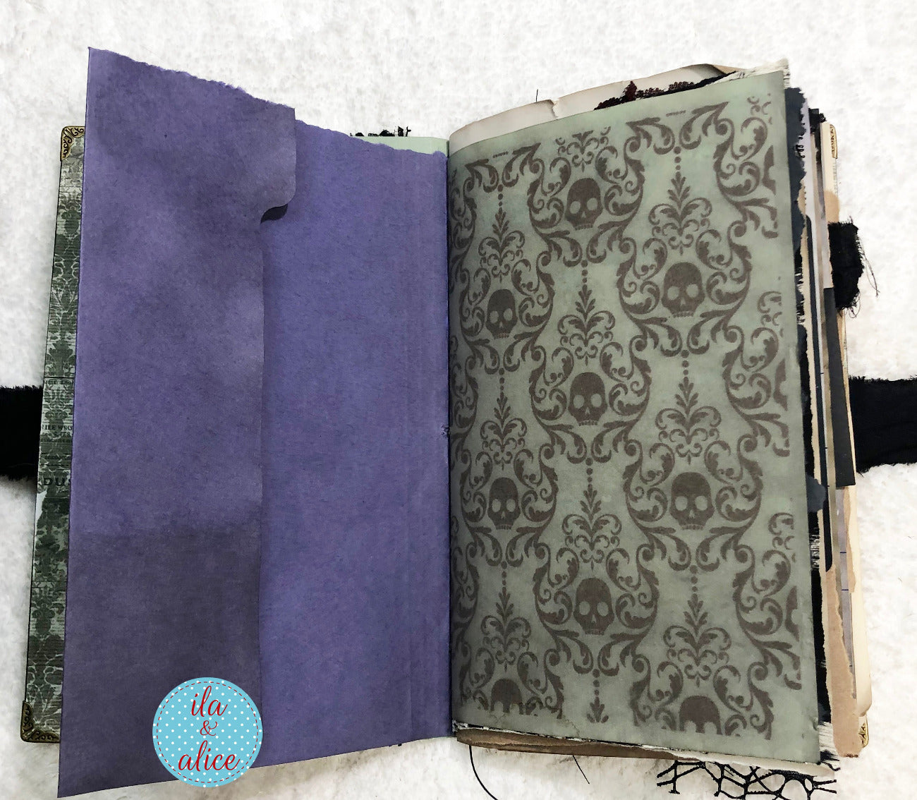 Handmade Eerie Halloween Gothic junk journal  with purple interior page and skull patterned cover on a textured surface.