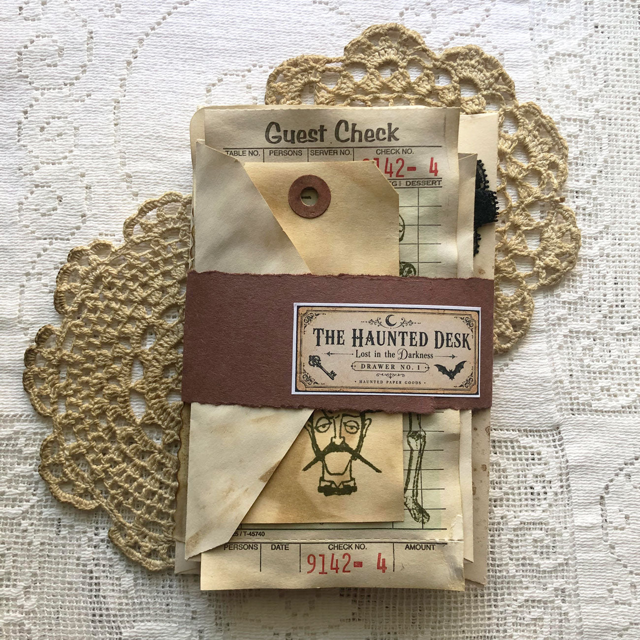 Wrapped haunted ephemera pack with coffee-dyed papers, tags, lace, and The Haunted Desk label.