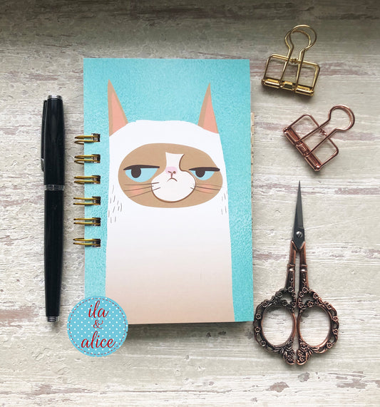 Mini handmade junk journal with minimalist grumpy cat illustration on blue background, spiral bound notebook