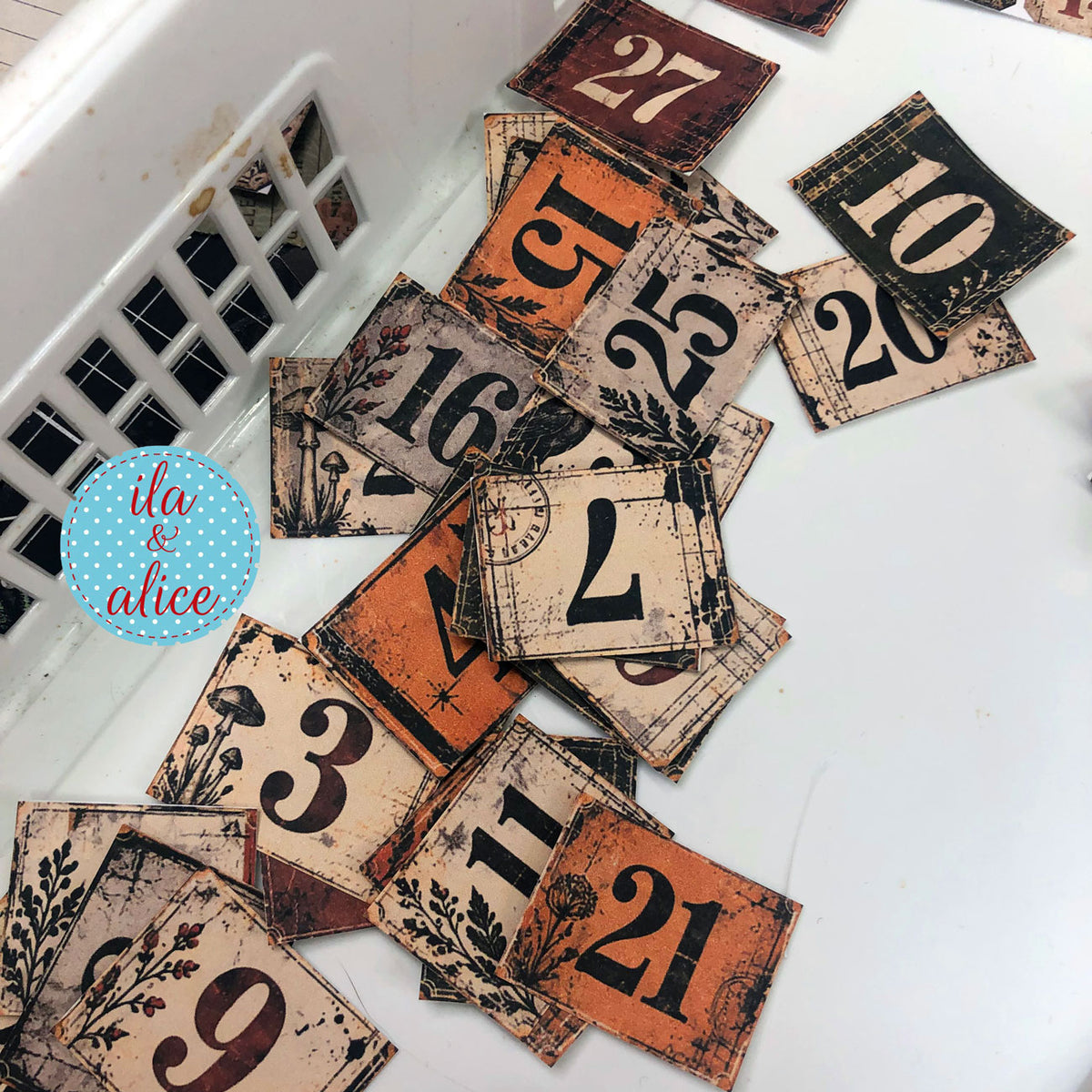 Cut Autumn Findings number tiles in orange, cream, olive, grey and brick red arranged beside a white basket.