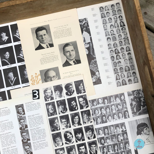 An open vintage yearbook or photo album spread, showing multiple printed pages filled with black-and-white portrait photographs, names, and text. The pages are arranged inside a wooden tray or box.