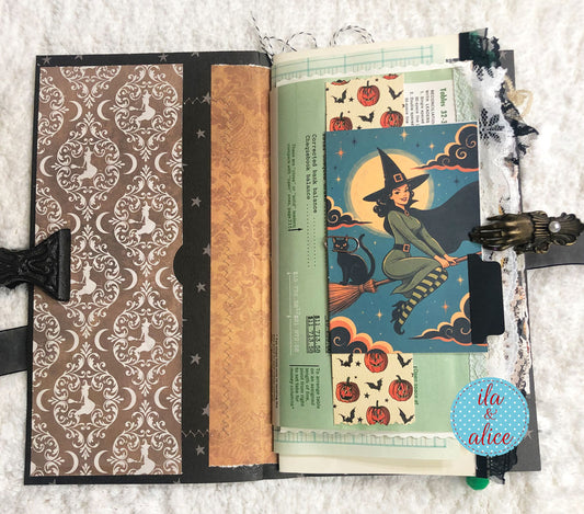 A handmade Halloween-themed scrapbook journal spread open on a white textured fabric background. The left page features a brown damask pattern with white cats, a gold patterned strip, and black stars.