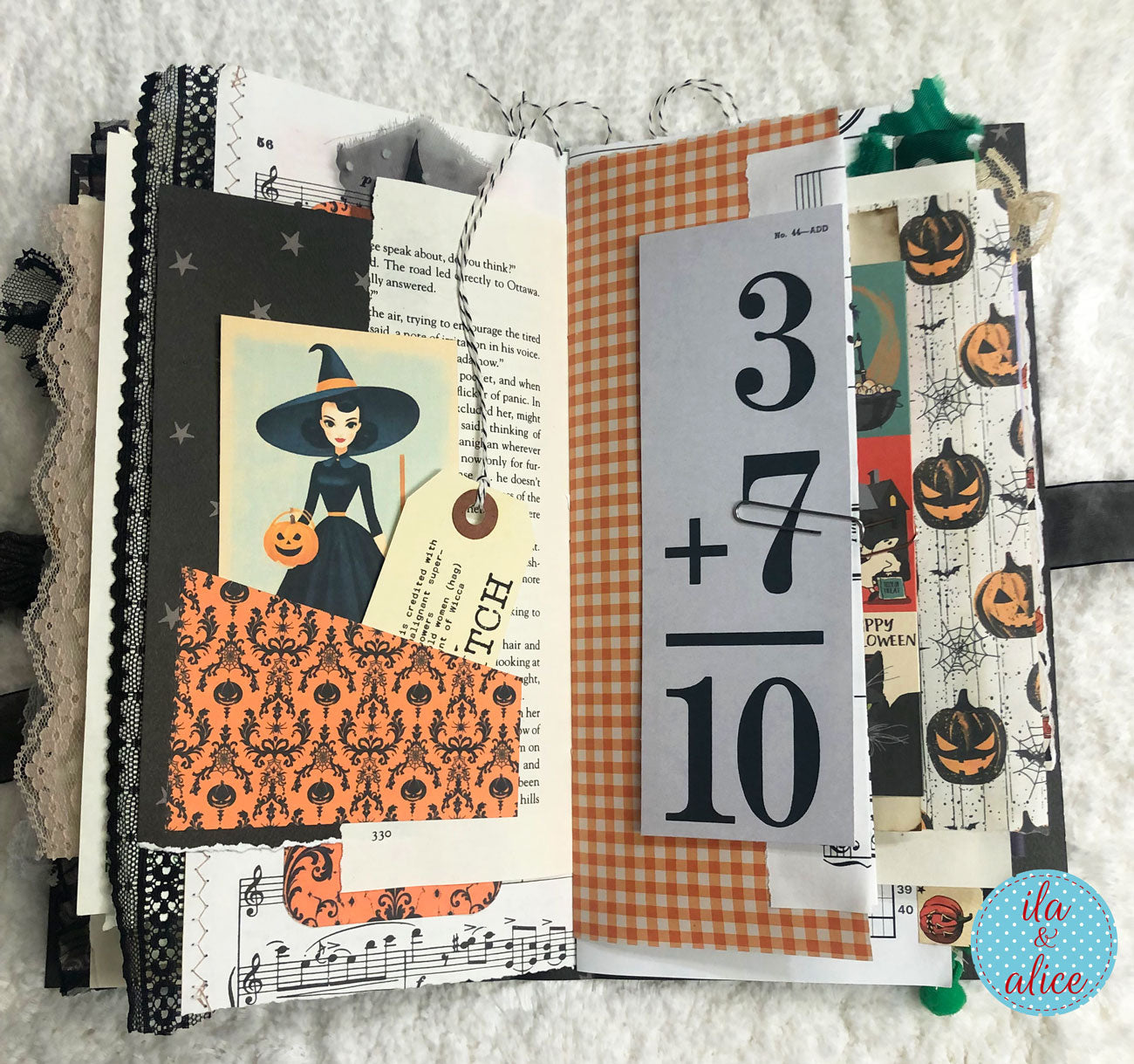 An open handmade journal or scrapbook album with layered Halloween-themed pages, including a witch illustration, orange patterned paper, black-and-white number collage, and pumpkin prints, photographed on a white textured fabric background.