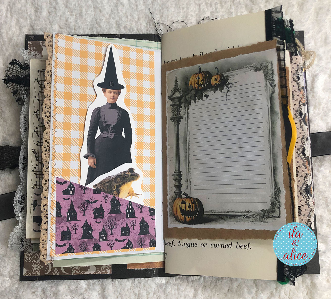 An open handmade scrapbook journal with Halloween-themed pages, featuring a witch cutout, a purple cat-patterned section, and a lined note card decorated with pumpkins. The journal is laid flat on a white textured fabric background.