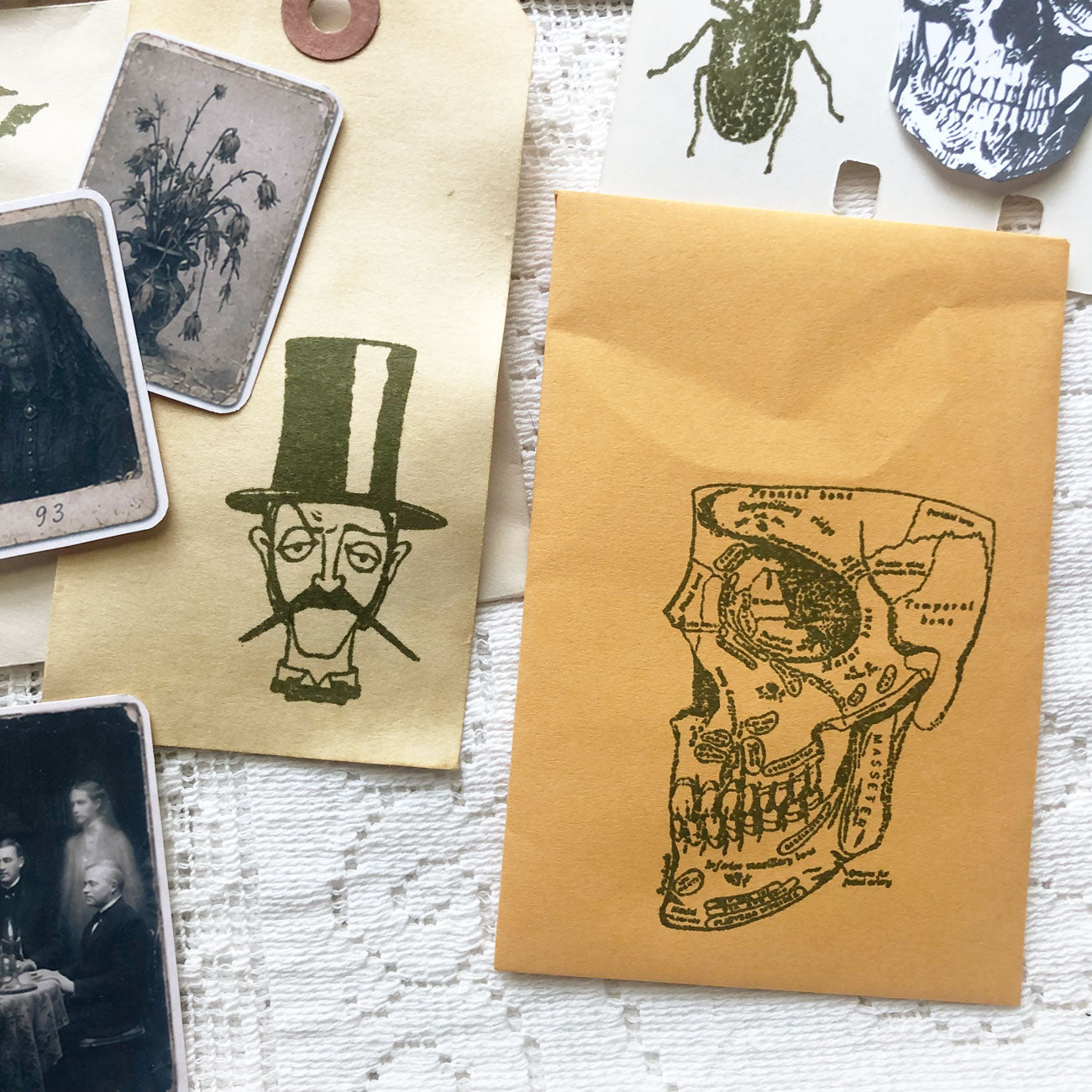 Close-up of gothic junk journal supplies including coffee-dyed tags, spooky stamps, and vintage-style portraits.