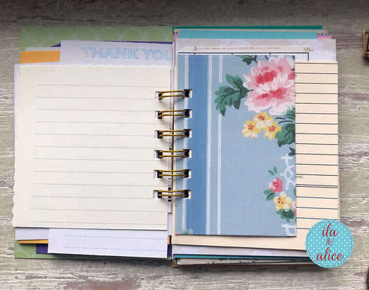 Planner with various pages including lined paper, a floral design, and a 'Thank You' card on a wooden surface.