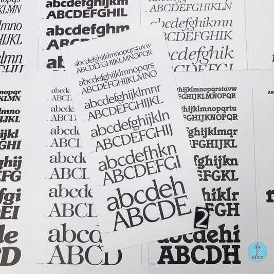 Several white book pages scattered on a white background, each printed with repeated black uppercase and lowercase alphabet lettering in varying font styles. A small circular logo in the bottom-right corner reads 'ila and alice'.